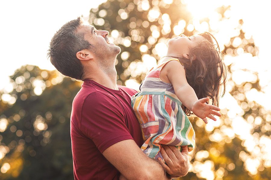 About Our Agency - Father Holding His Young Daughter Outside On Warm Day