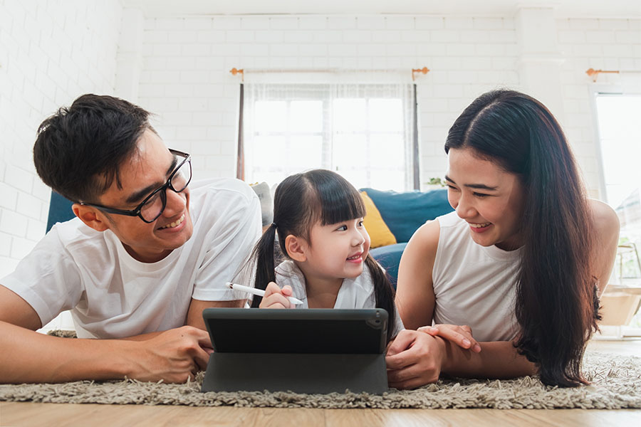 Client Center - Smiling Family Laying On The Floor At Home Using A Tablet Together